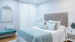 Ein Schlafzimmer mit Bett, Bank, Nachttisch und Spiegel.