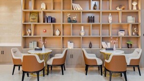 A modern dining area with a wooden bookshelf filled with books and decorative items, and a seating arrangement of four chairs around two round tables.