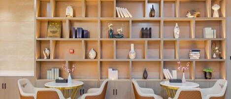 A modern dining area with a wooden bookshelf filled with books and decorative items, and a seating arrangement of four chairs around two round tables.