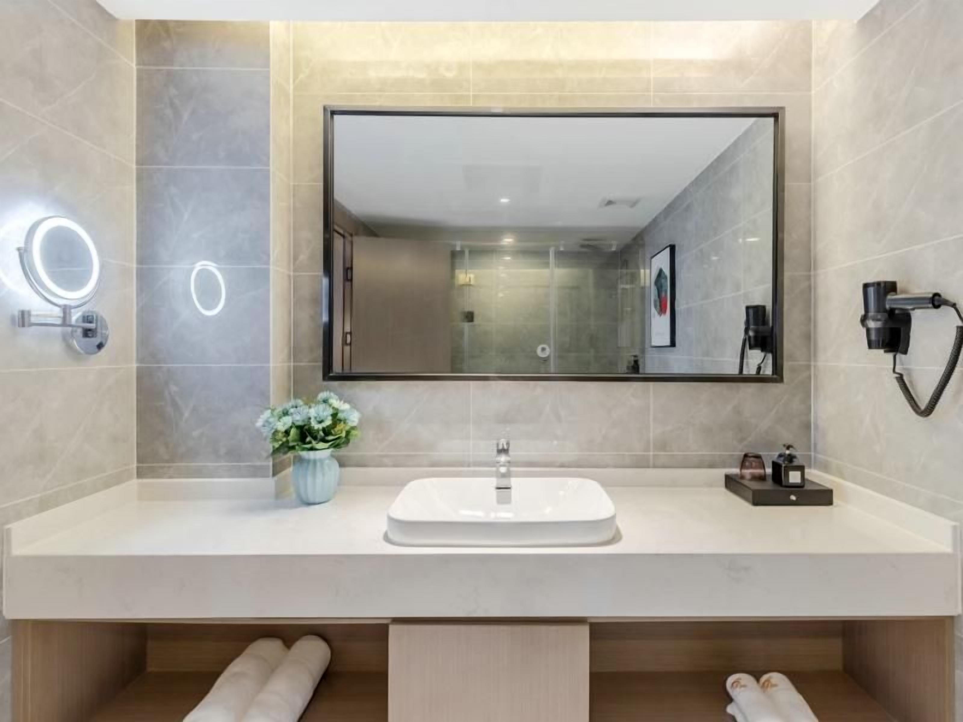 A modern bathroom with a large mirror, a sink, and a hairdryer mounted on the wall.