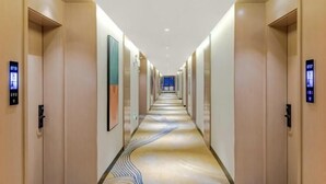 A modern hotel corridor with a patterned carpet, wooden walls, and elevator buttons.