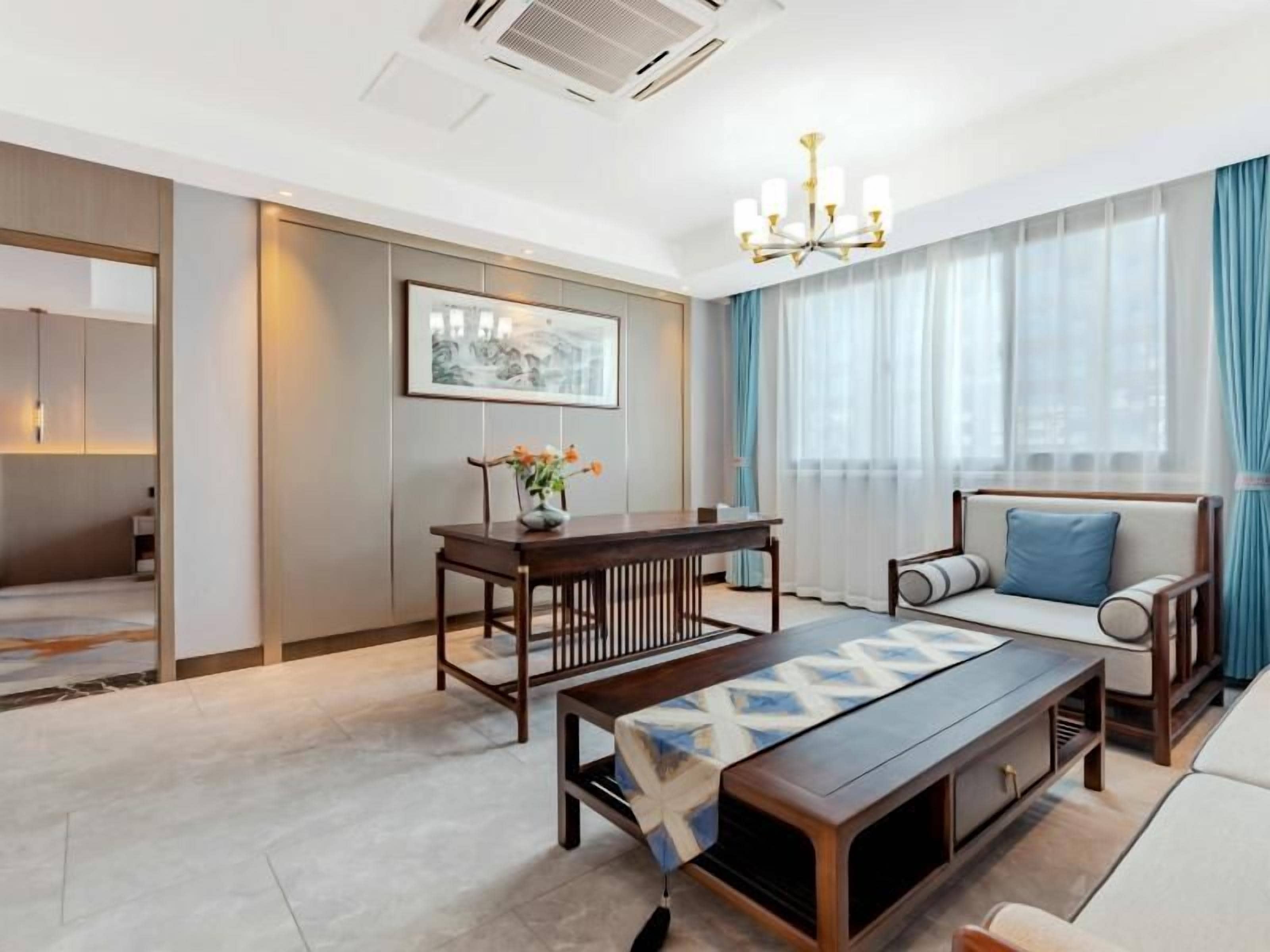 A modern hotel room with a dining table, sofa, and a large window with curtains.