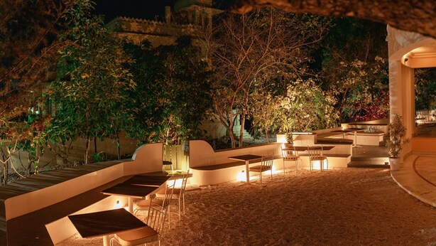 An outdoor seating area with tables and chairs, surrounded by trees and a building in the background. - Devraj Villa-A Luxury Homestay with Pool (Udaipur)