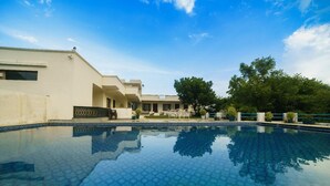 A swimming pool with a geometric tile pattern, surrounded by a building with a flat roof and a balcony. - Devraj Villa-A Luxury Homestay with Pool (Udaipur)