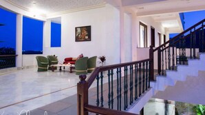 A spacious living area with a staircase, green chairs, and a painting on the wall. - Devraj Villa-A Luxury Homestay with Pool (Udaipur)
