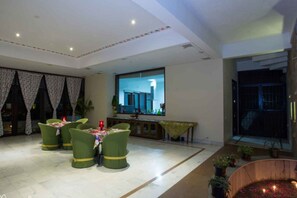 A dining area with green chairs and a table set for four, a small table with a yellow tablecloth, and a decorative water feature with flowers. - Devraj Villa-A Luxury Homestay with Pool (Udaipur)