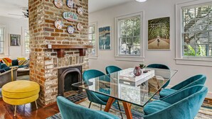 Un comedor con chimenea de ladrillo, sillas color turquesa y una mesa de vidrio.