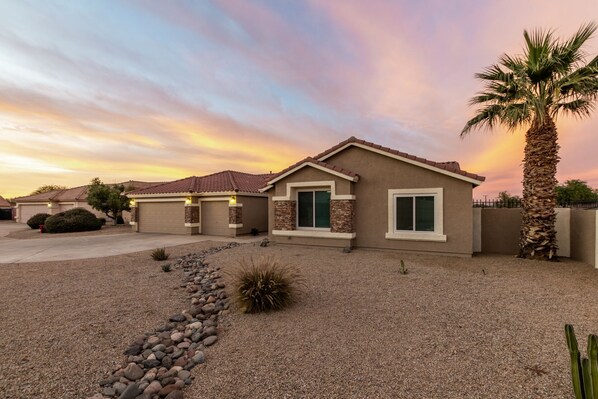 A single-story house with a tiled roof, a front garage, and a landscaped front yard with a palm tree and a rock garden.