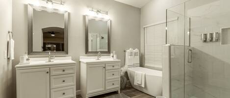 A modern bathroom with two sinks, a glass shower enclosure, and a vanity with drawers.