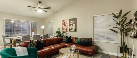 A living room with a brown leather sectional sofa, green armchairs, a round coffee table, and a ceiling fan.