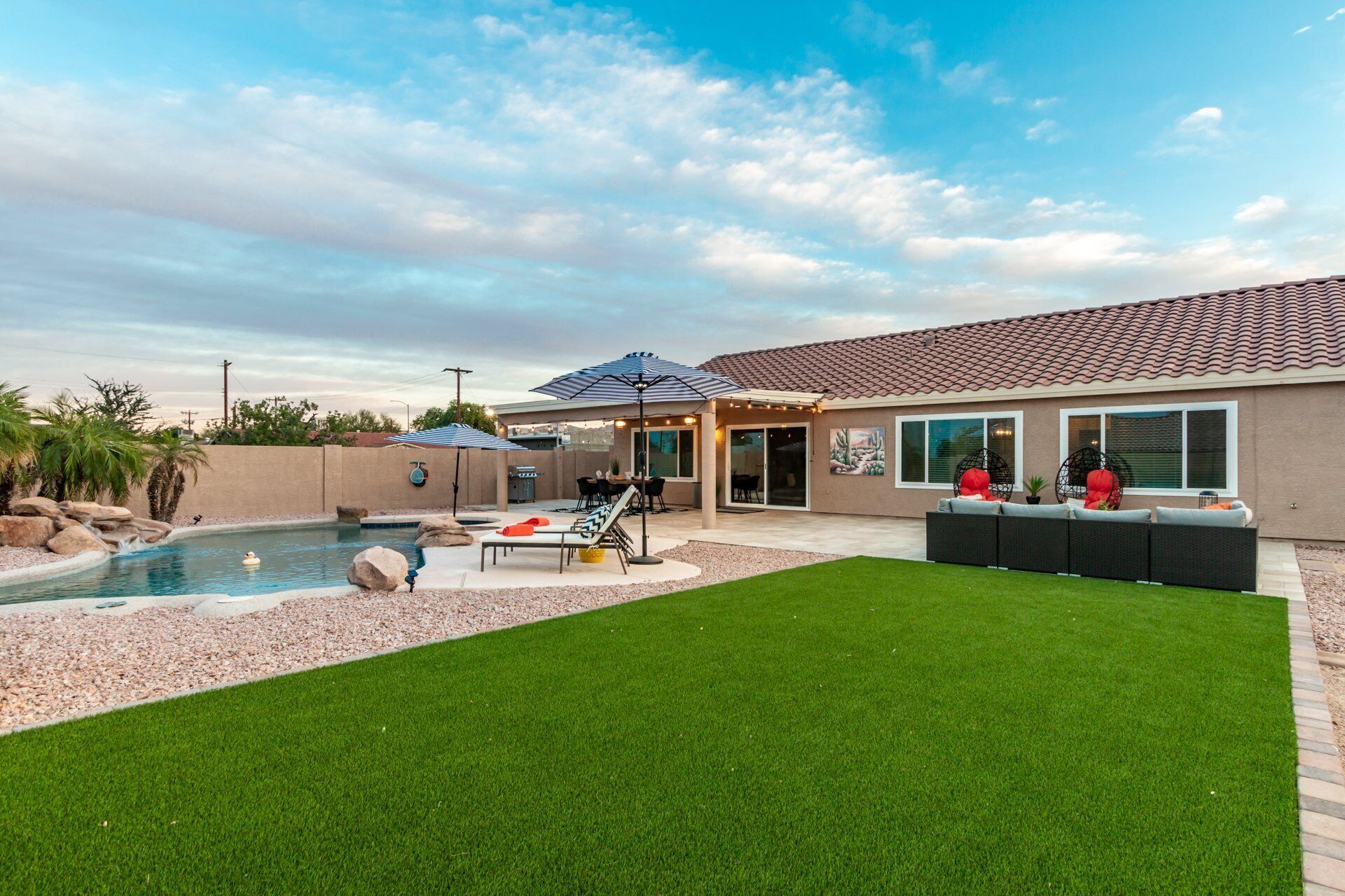 Un patio trasero con piscina, zona de patio amueblada al aire libre y espacio de estar cubierto.