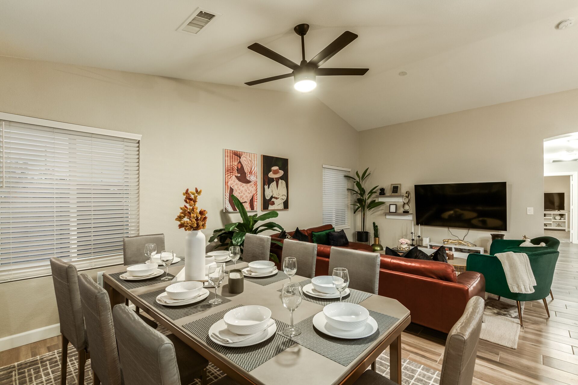 A dining area with a table set for four, a ceiling fan, and a TV in the background.