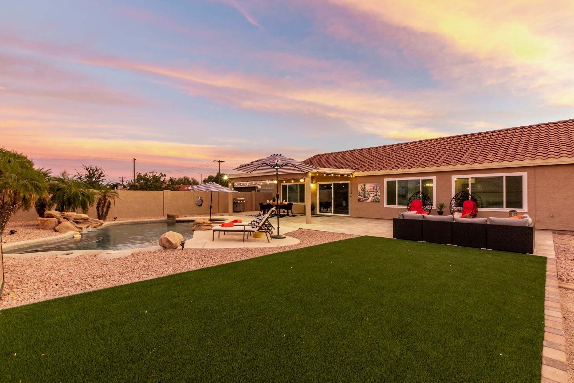 A backyard with a swimming pool, patio furniture, and a covered seating area.