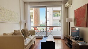 A modern living room with a sofa, a coffee table, a TV, and a balcony with chairs. - Palermo, Las Cañitas. In front of the Polo field. (Buenos Aires)