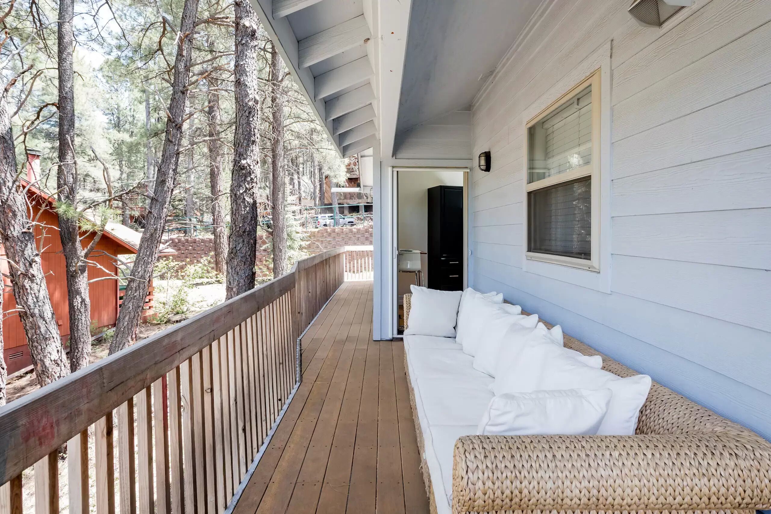 A wooden deck with a white sofa and wicker furniture, overlooking a forested area.