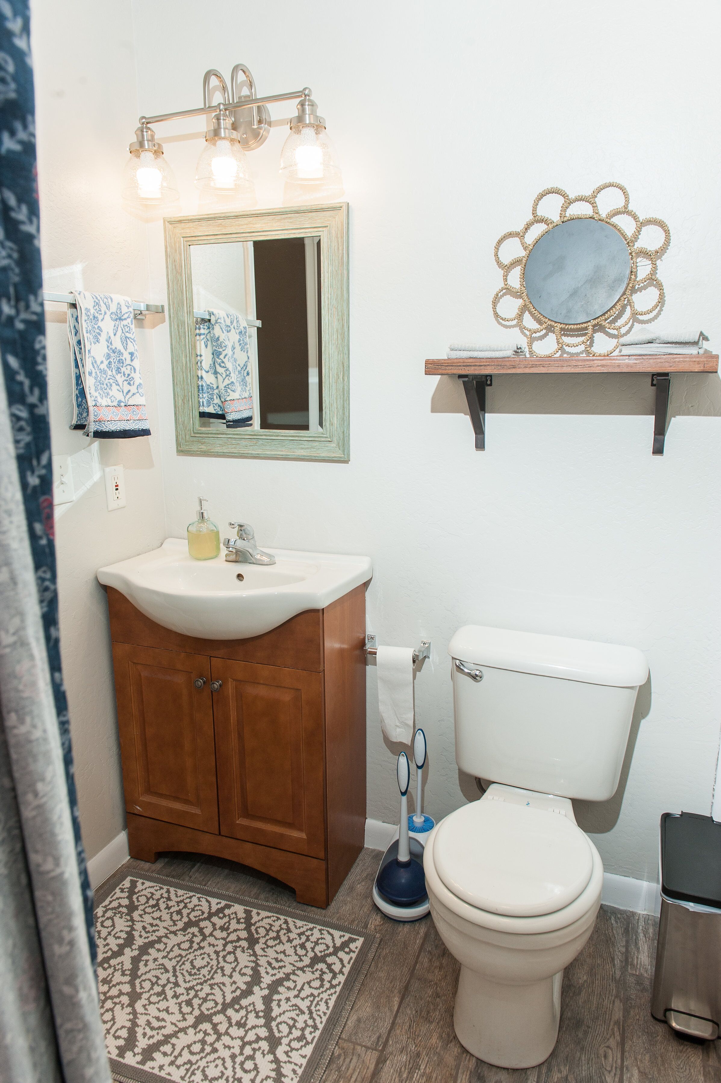 A bathroom with a wooden vanity, a white sink, a mirror, a toilet, and a patterned rug.