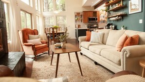 A spacious living room with a sofa, armchair, and coffee table, a dining area with chairs and a table, and a kitchen with appliances and shelves. - The Toho-Tally Toho-Tel (Flagstaff)