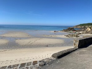 A beach with a stone wall in the foreground and rocky terrain on the right. - Seaside house (PRIMELIN)