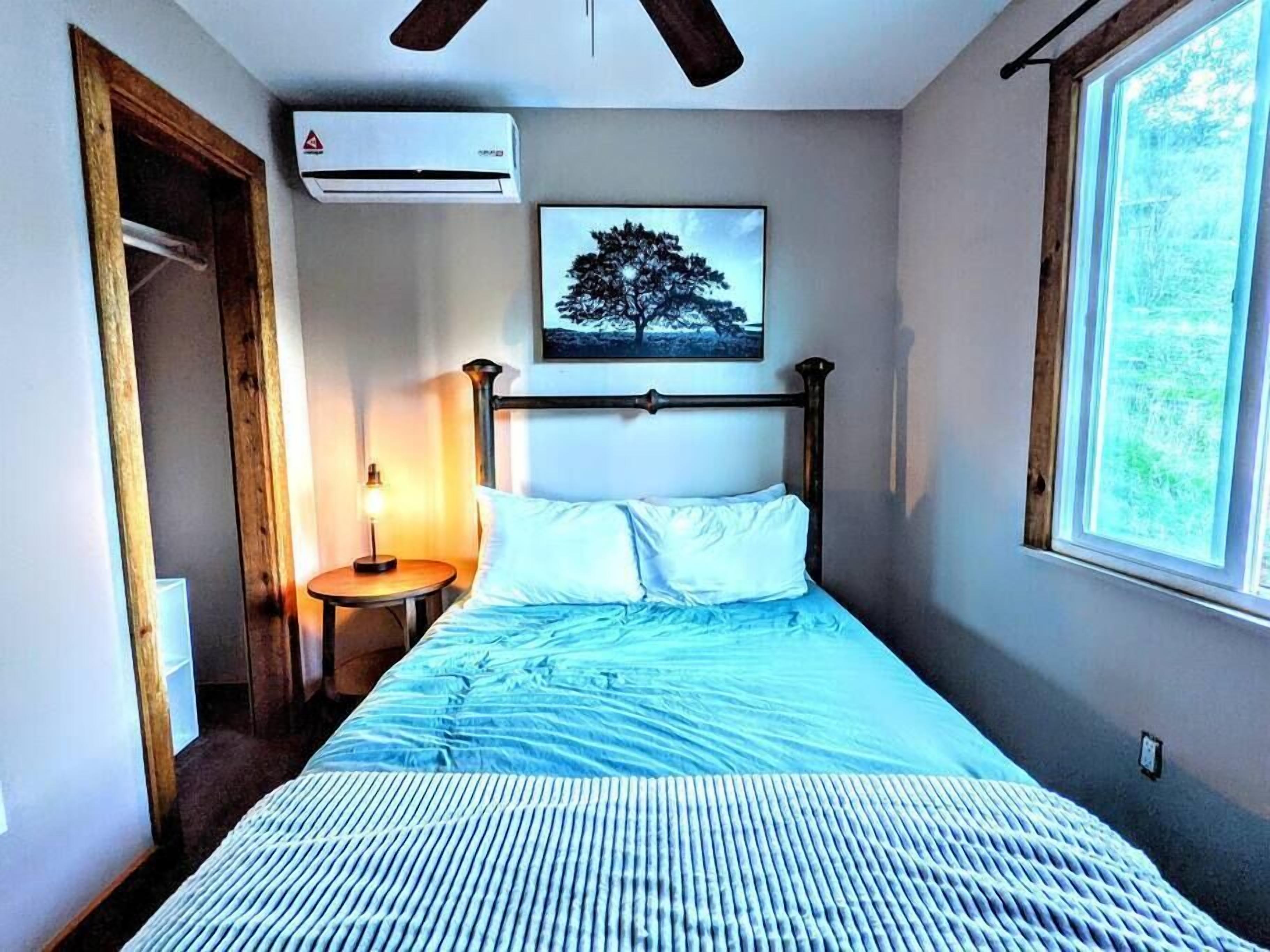 A bedroom with a bed, a nightstand, a wall-mounted air conditioner, a window, and a door.