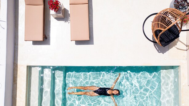 A rectangular pool with clear water, a lounge chair, and a wicker chair. - Pink Freud Villas Santorini (Santorini)