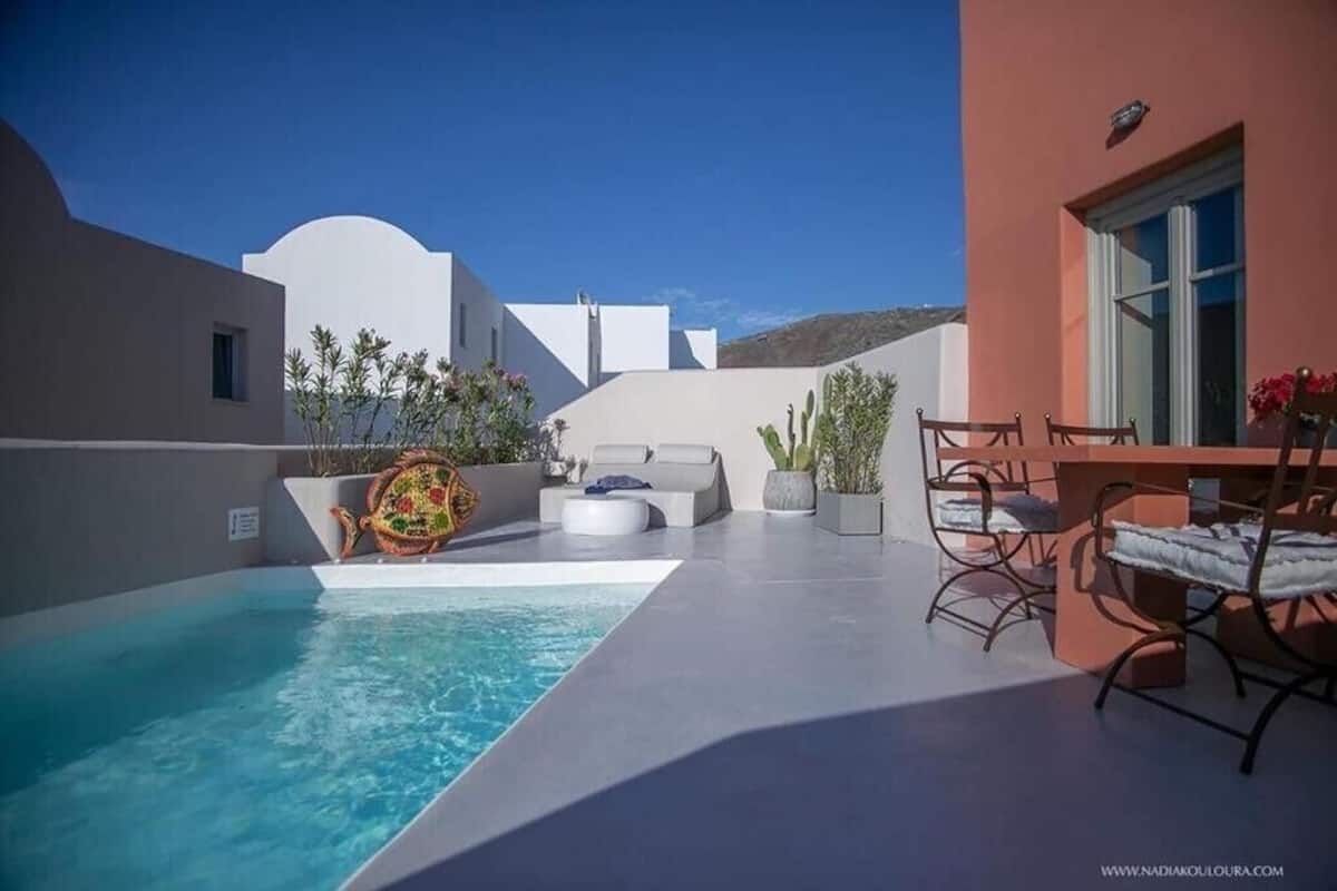 Zona de piscina con una pileta blanca, una mesa de madera con sillas y un sofá blanco.
