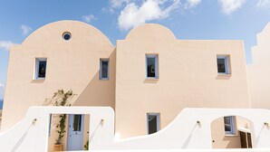 A building with a curved facade, multiple small windows, and a potted plant in the foreground. - Pink Freud Villas Santorini (Santorini)