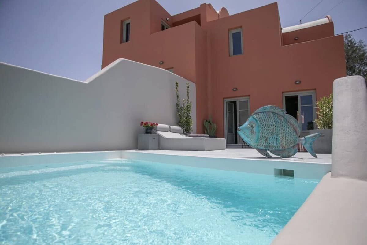 Un área de piscina moderna con una piscina azul cristalina, un borde de piscina infinita blanco y una gran escultura decorativa de un pez.