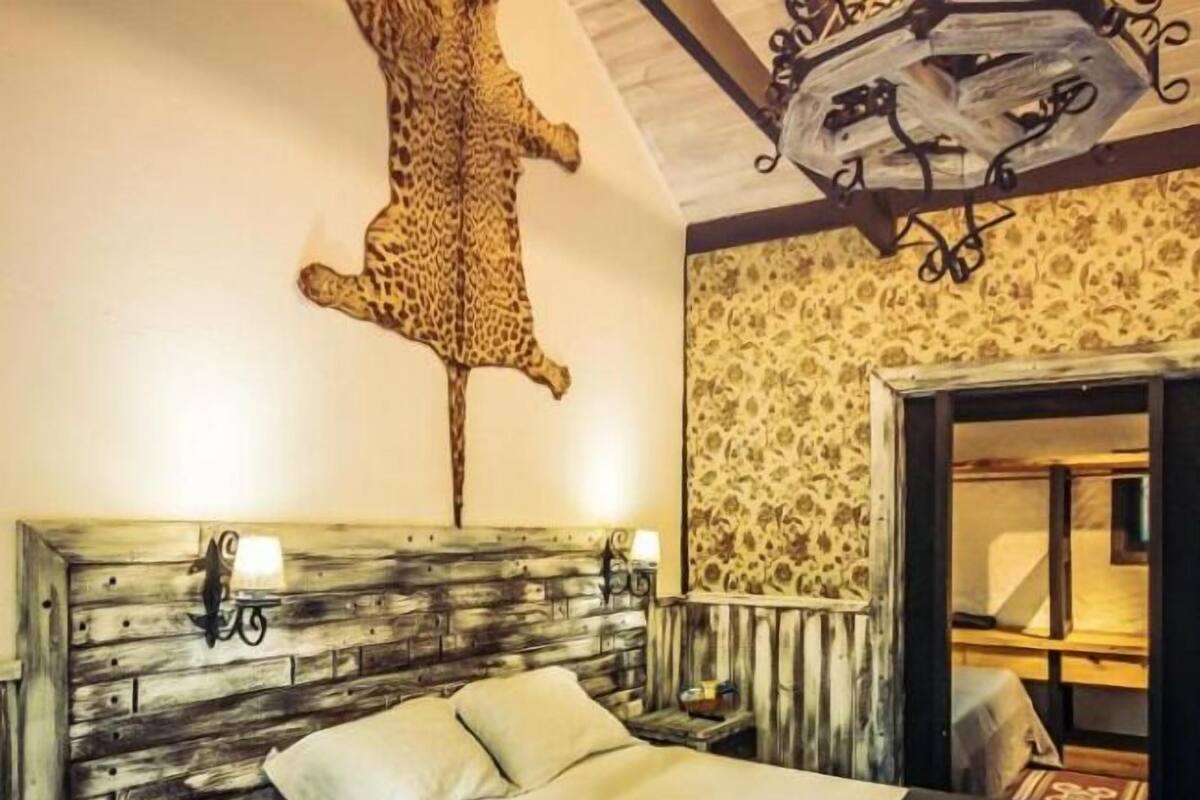 A bedroom with a wooden headboard, a mounted animal hide, two bedside lamps, and a bed with a white and blue bedspread.