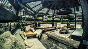 A rustic outdoor seating area with stone tables and benches, surrounded by greenery and a wooden pergola. - Art Lodge Campos do Jordão (Campos do Jordão)