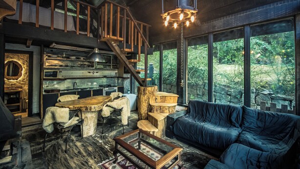 A rustic interior with a loft bedroom, a dining area, and a large window overlooking greenery. - Art Lodge Campos do Jordão (Campos do Jordão)