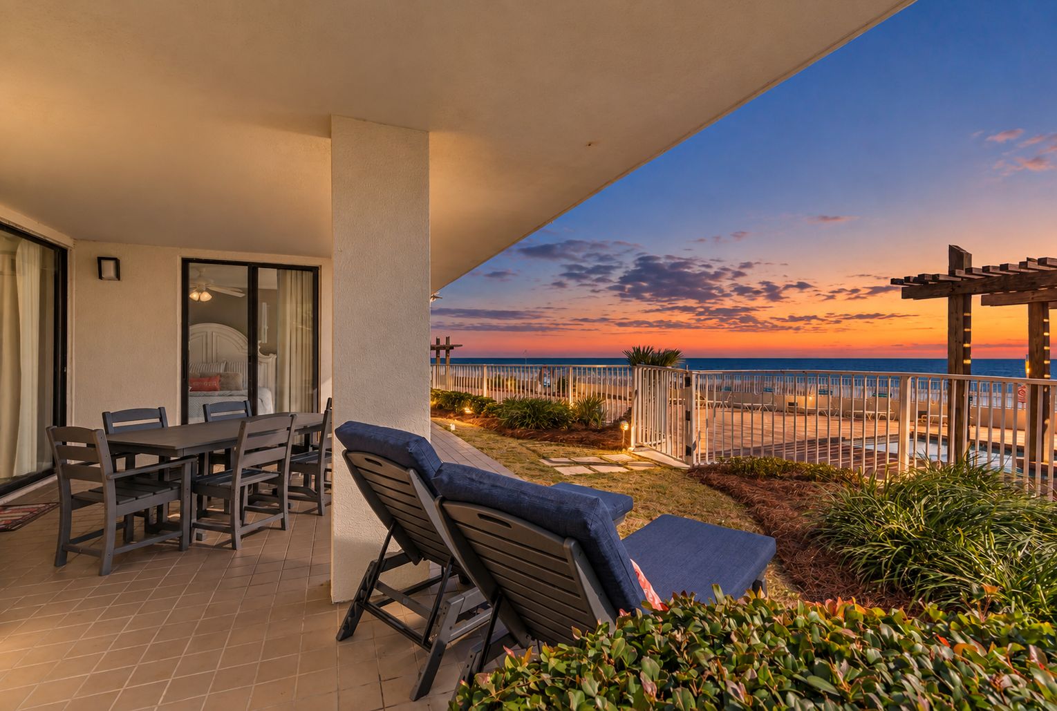 A terrace with a table and chairs, a covered seating area, and a view of the sea at sunset.