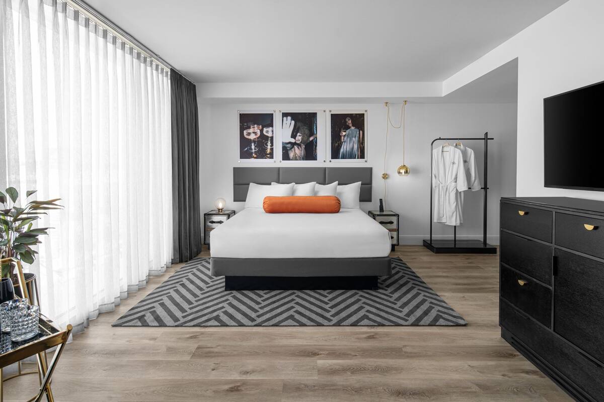 A modern bedroom with a large bed, a TV, a wardrobe, and a bedside table.