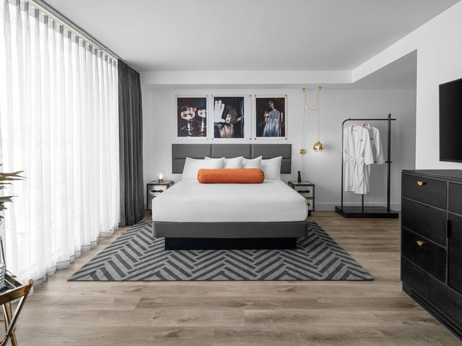 A modern bedroom with a large bed, a TV, a wardrobe, and a bedside table.
