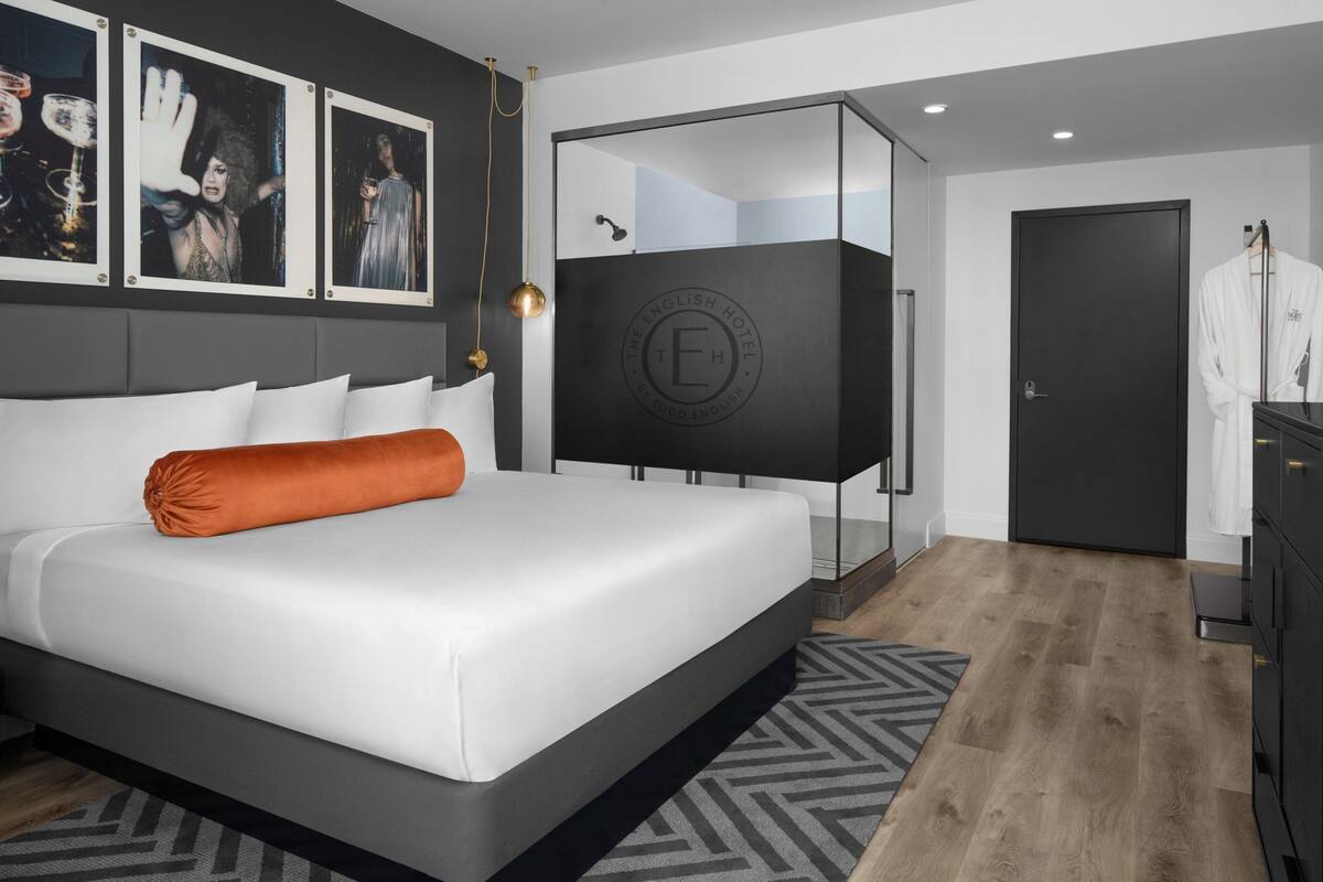 A modern hotel room with a large bed, a mirror, a wardrobe, and a door.