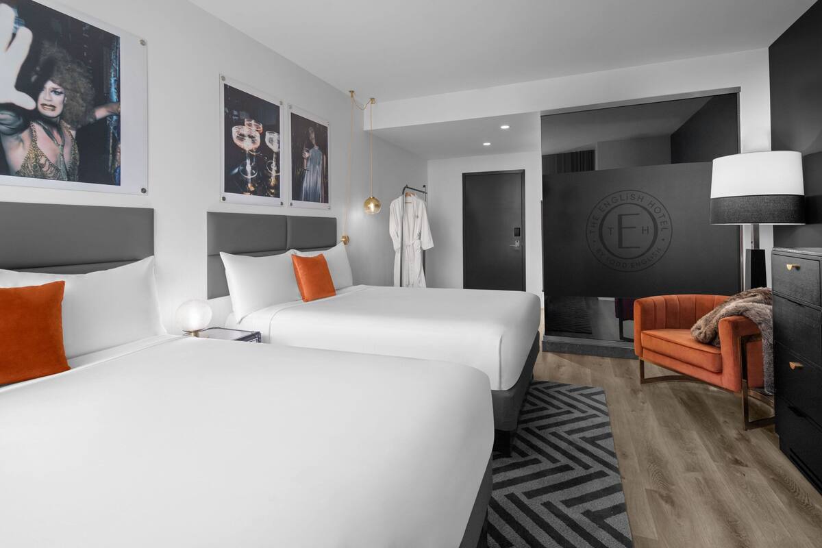 A modern hotel room with two beds, a seating area, and a wardrobe.