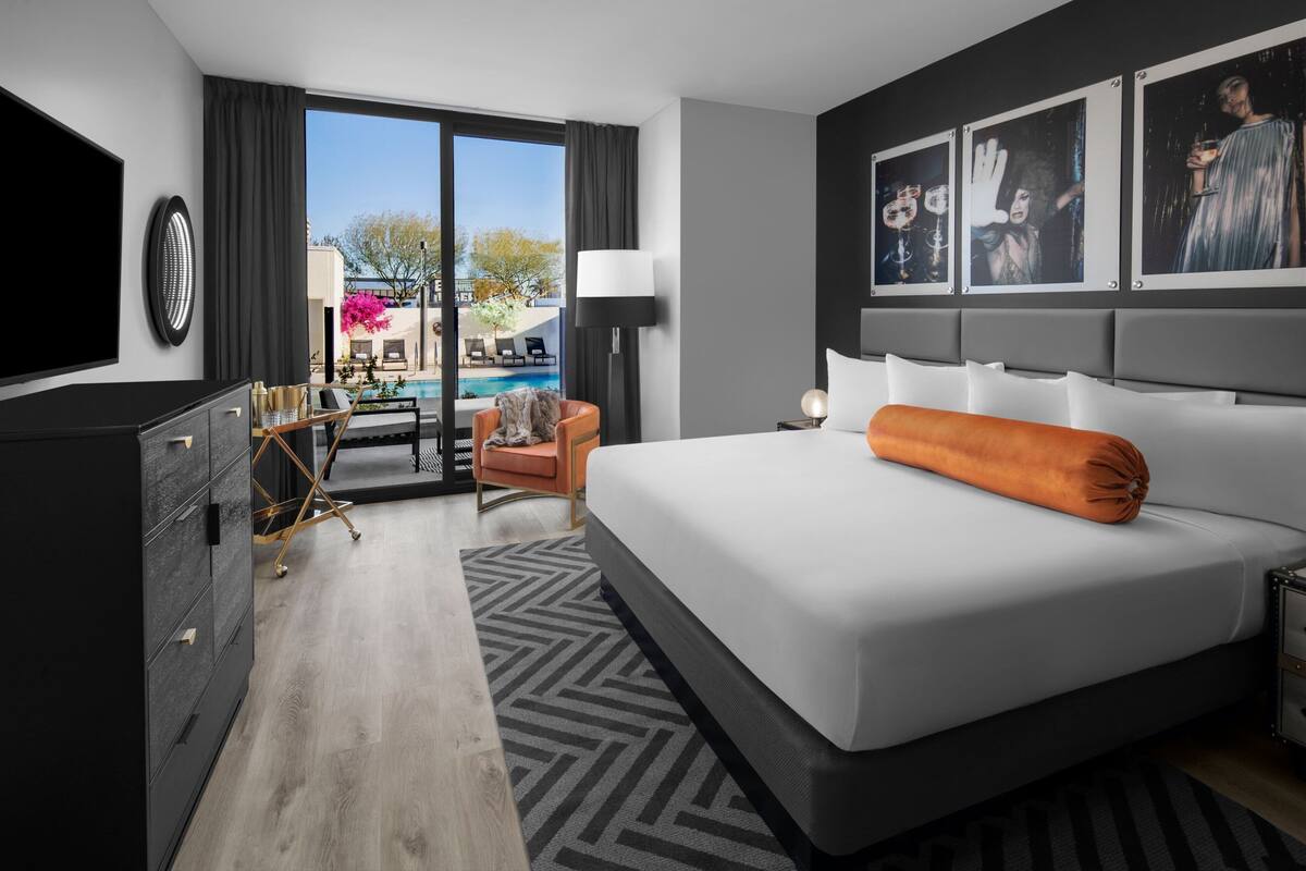 A modern hotel room with a large bed, a TV, a desk with a chair, and a view of a swimming pool.
