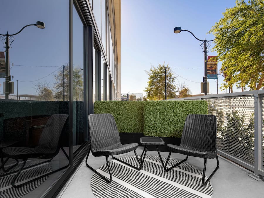 A modern outdoor seating area with two chairs and a small table, a glass partition, and a green hedge wall.