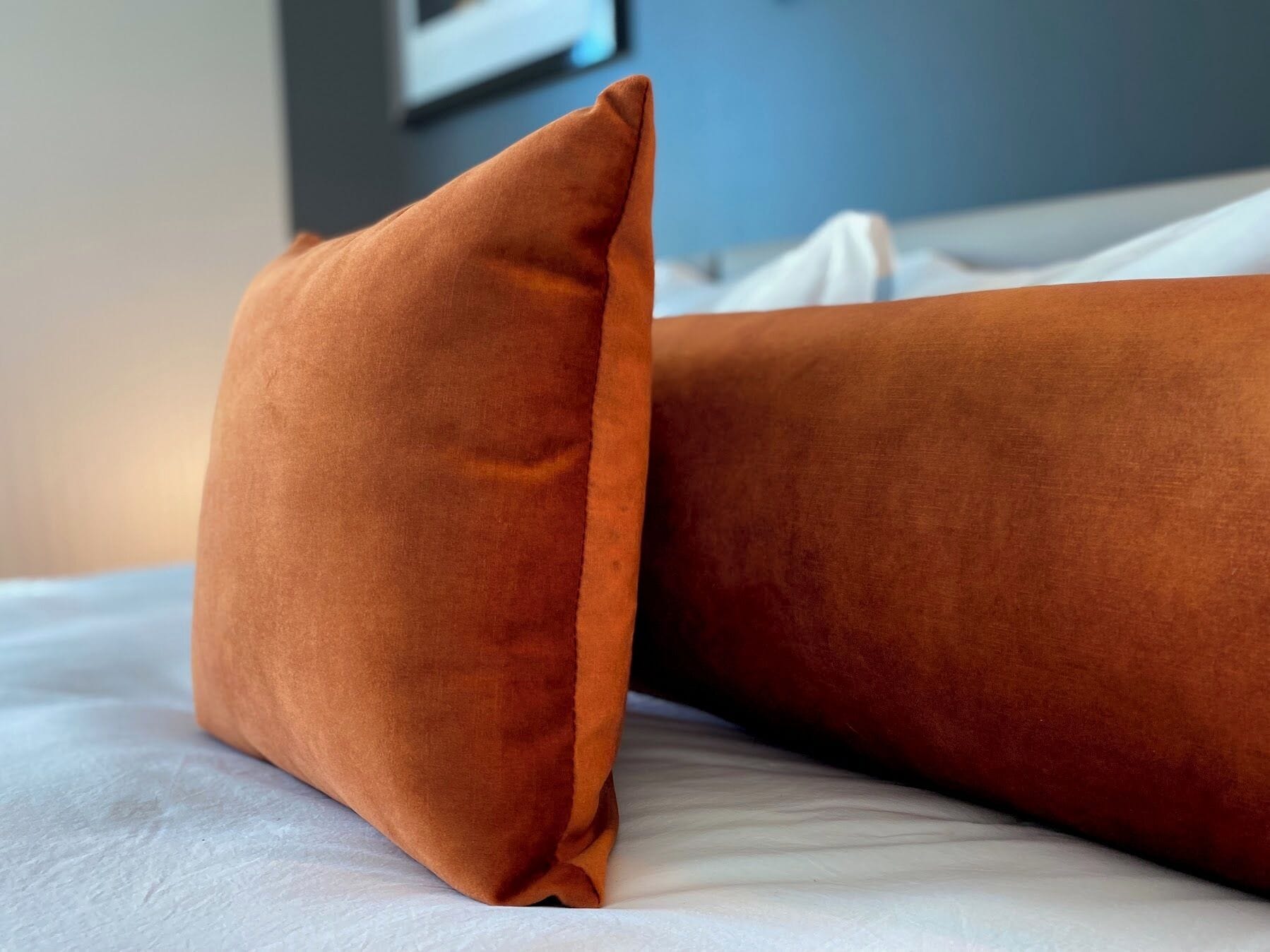 Una cama con sábana blanca y una almohada naranja.