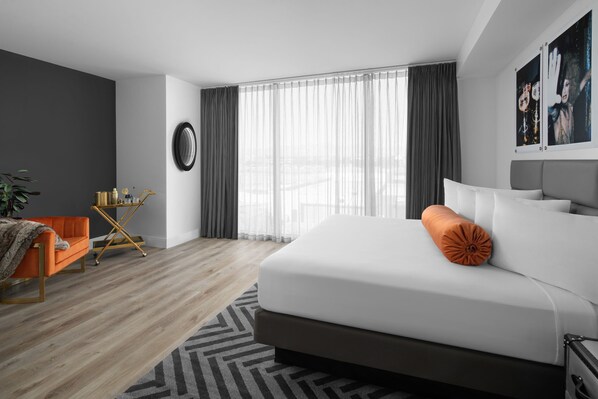 A modern hotel room with a large bed, a small orange armchair, a side table, and a large window with sheer curtains. - The ENGLISH Hotel, Las Vegas, a Tribute Portfolio Hotel, 21 and over (Las Vegas)