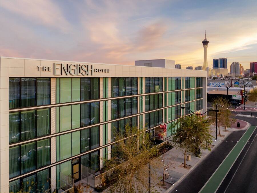 A modern hotel with a glass facade, located in a city with a prominent tower in the background.