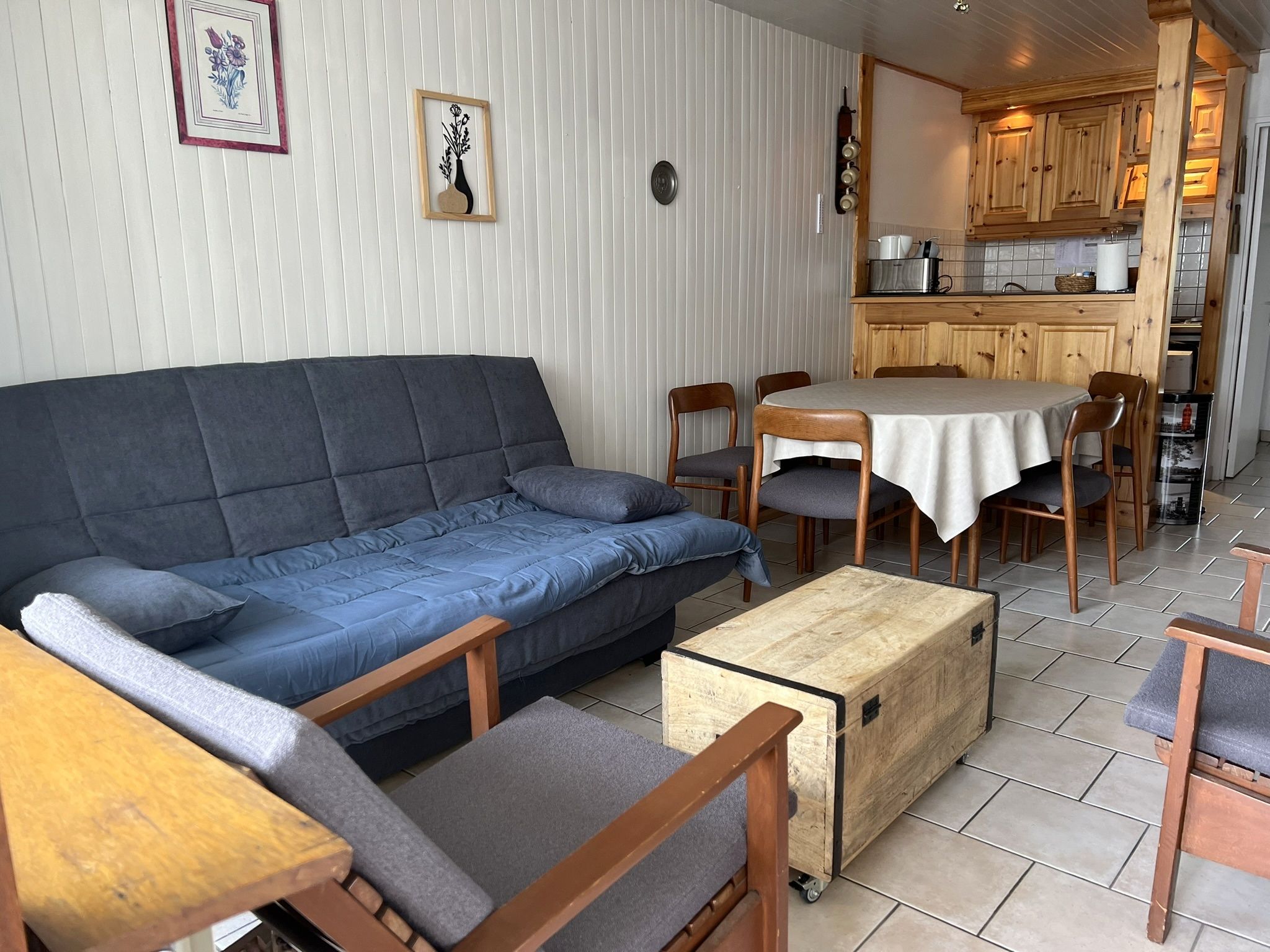 Un salon comprenant un canapé, des fauteuils, une petite table et un coin cuisine avec des meubles en bois et un fourneau.