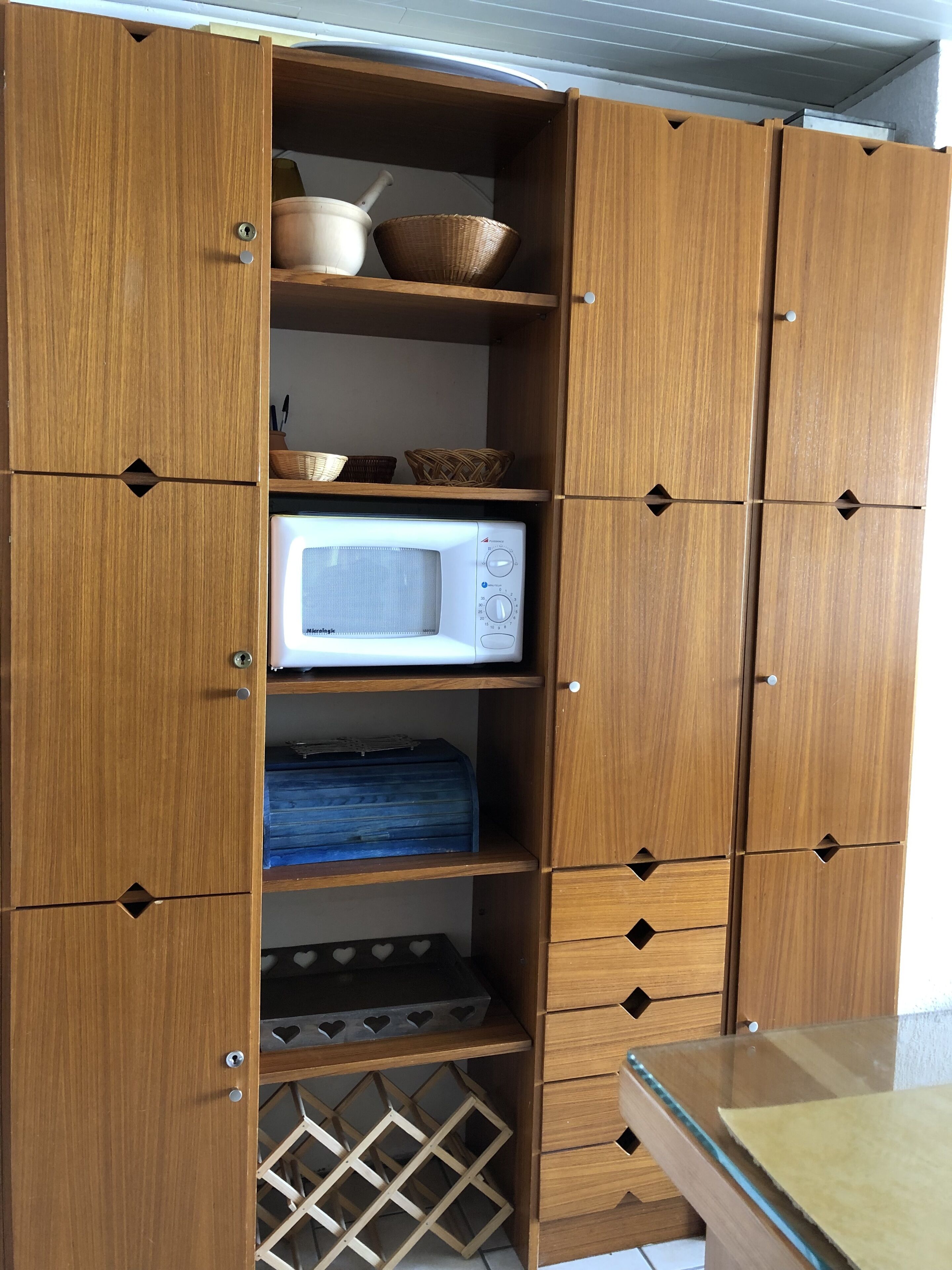 A wooden cabinet with multiple shelves, a microwave, and a wine rack.