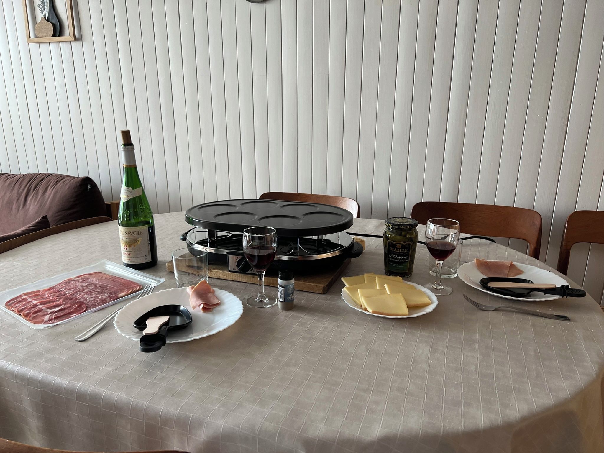 Una mesa de comedor con una plancha para gofres, platos de comida, copas de vino y una botella de vino.