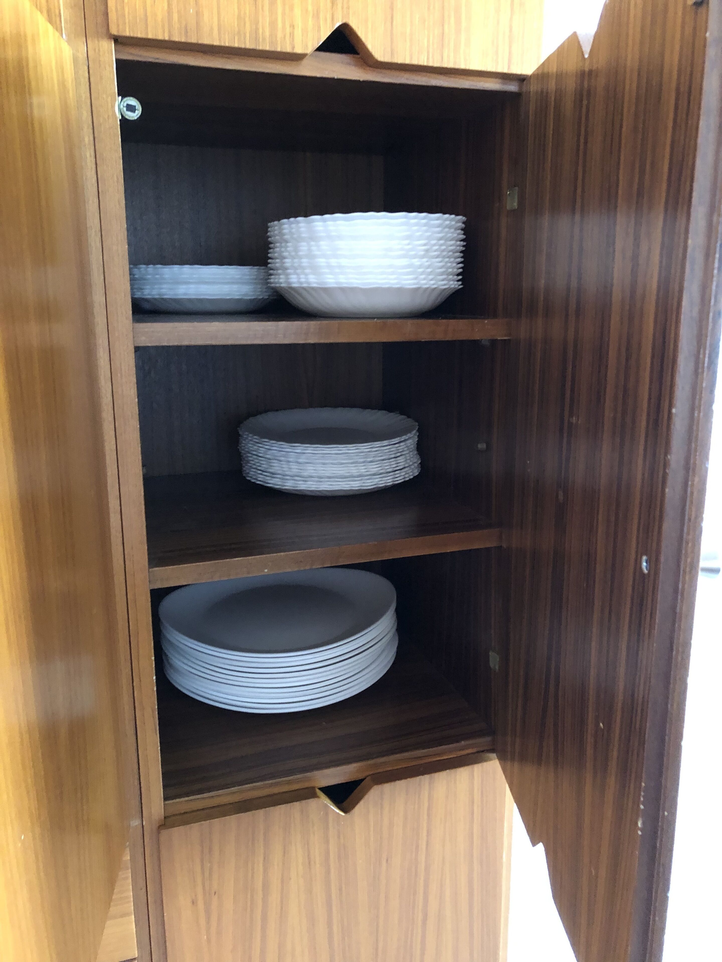 A wooden cabinet with three shelves, each holding stacks of white plates.