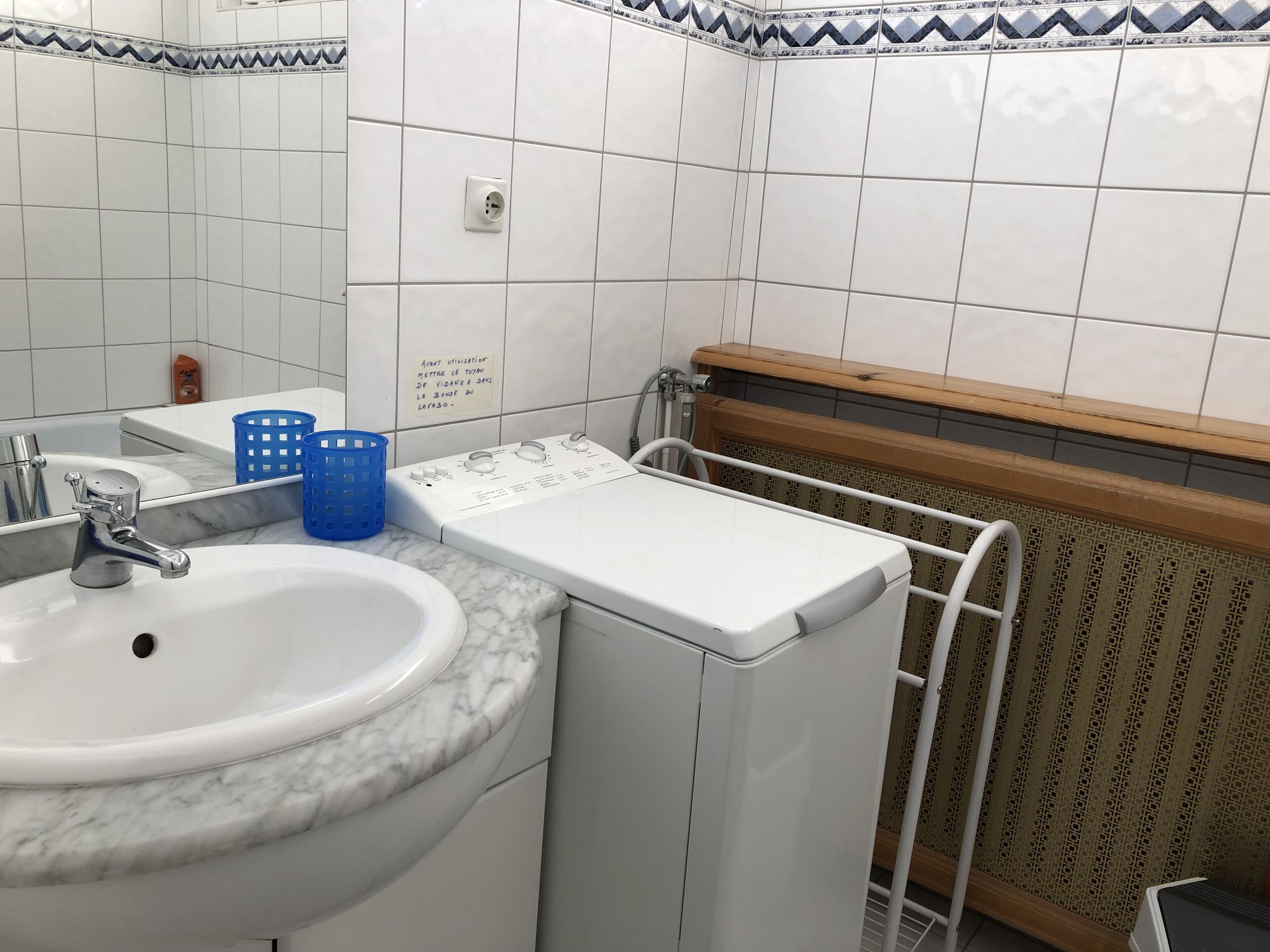Casa de banho com lavatório, espelho e máquina de lavar roupa.