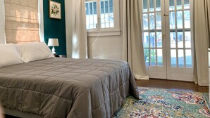 A bedroom with a bed, a nightstand, a lamp, a window with curtains, and a view of the outside. - Sunny Stifft’s Station/Capital View: Off Street Parking AT&T Fiber (Little Rock)
