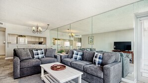 Un salon moderne avec des canapés gris, une table basse blanche et un téléviseur.