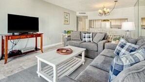 Un salon moderne avec un téléviseur à écran plat, une table basse en bois et un ensemble de canapés gris.