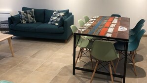A modern living room with a teal sofa, a wooden coffee table, and a dining table with colorful chairs. - Charming seaside house with enclosed garden (Bernières-sur-Mer)