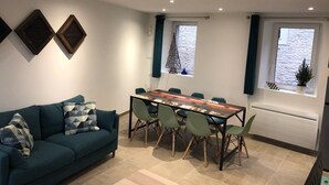 A modern living room with a sofa, a dining table with chairs, and two windows with curtains. - Charming seaside house with enclosed garden (Bernières-sur-Mer)